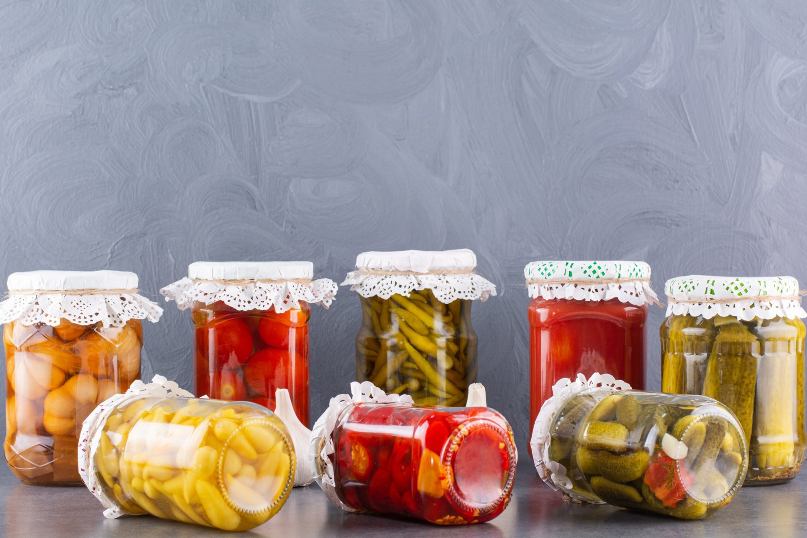 Glass jars of pickled cucumbers and tomatoes on stone background. High quality photo